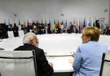 People seated around a large round table, flags behind.