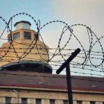 Luxury Meals Smuggled In — Prison Scandal Unfolds Barbed wire in front of a prison tower.