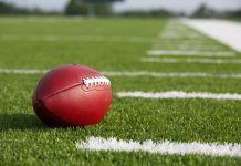 Scandal Erupts: Champion Coach’s Shocking Downfall A red American football resting on a green artificial turf field
