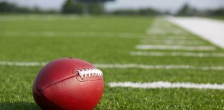 Scandal Erupts: Champion Coach’s Shocking Downfall A red American football resting on a green artificial turf field