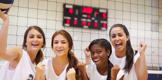 Four female volleyball players celebrating in a gymnasium