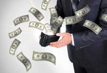 A businessman holding a wallet with money flying out