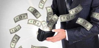 A businessman holding a wallet with money flying out