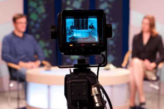 Camera focused on a television studio interview with two seated hosts