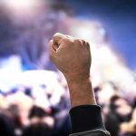 ICE Officer’s Fatal Shot Ignites Protest Chaos Raised fist in a crowd at night.