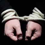 Hands tied with rope in the dark.