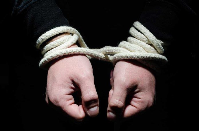 155804528 Hands tied with rope in the dark.