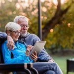 Shocking Genetic Twist: Aging Truths Shattered Older couple sitting on bench using tablet outdoors