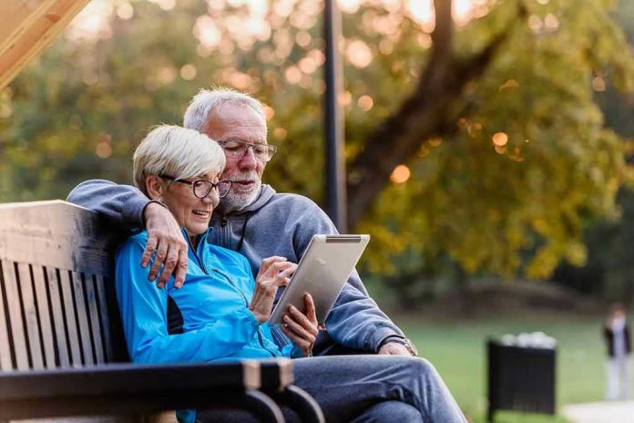 Older couple sitting on bench using tablet outdoors