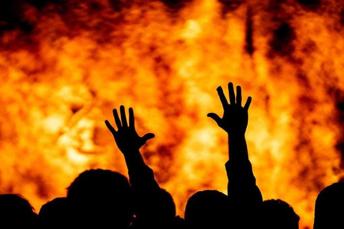 Silhouetted hands raised against a fiery background.