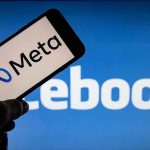 Meta on phone screen, Facebook in background.