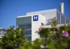 Modern hospital building with a prominent H sign against a clear blue sky