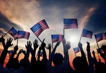Silhouetted crowd holding American flags against a sunset sky