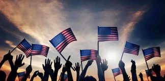 Silhouetted crowd holding American flags against a sunset sky