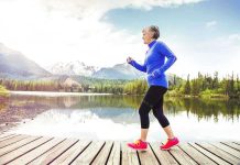 Senior woman jogging along a lakeside with mountains in the background