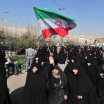 Group of women in black attire marching with an Iranian flag