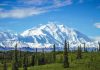 Snow-covered mountain under blue sky with green foreground.