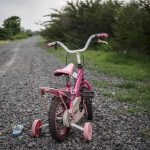 Police Doubt MISSING Toddler’s Parents Pink childrens bike with training wheels on gravel path.