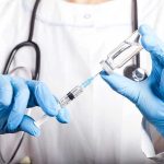 FDA Gatekeepers Hit Moderna With Rejection Doctor filling syringe with vaccine from vial.