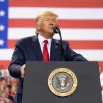 USA! Chants Rock Capitol After Trump’s Move Man speaks at podium with U.S. flag background.
