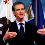 Newsom’s $239M Prison SPA Outrage Man speaking with flags in the background