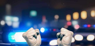 Hands in handcuffs in front of police cars.