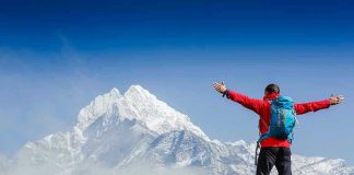 Hiker with arms outstretched in front of snowy mountains.