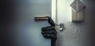 Gloved hand opening door with security chain.