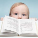 A curious baby peeking over an open book