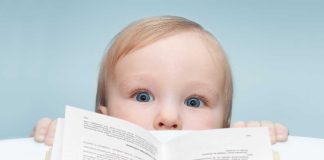 A curious baby peeking over an open book