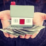 Hands holding a small house model and cash bills