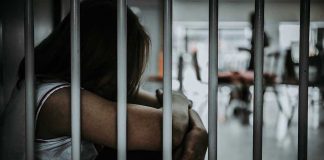 Person sitting behind bars with arms wrapped around knees.
