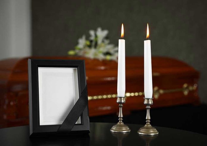 1480856555 Casket, photo frame, and two lit candles.