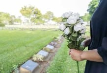 Person holding white roses at a cemetery.