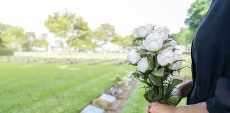 Person holding white roses at a cemetery.