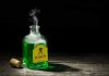 Mom Poisons Husband’s Cocktail—5x Lethal Dose! Green poison bottle with cork on wooden surface.