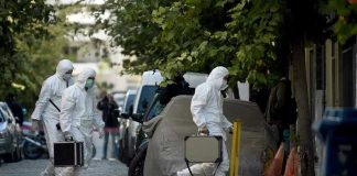 Investigators in hazmat suits carrying equipment cases.