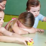 Children at a table with building blocks, one child appears upset