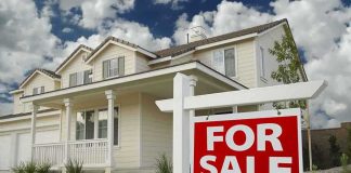A suburban house with a For Sale sign in the front yard