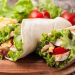 California Dictates Tortilla Ingredients Two chicken wraps filled with lettuce and tomatoes on a wooden plate with fries