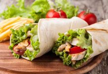 California Dictates Tortilla Ingredients Two chicken wraps filled with lettuce and tomatoes on a wooden plate with fries