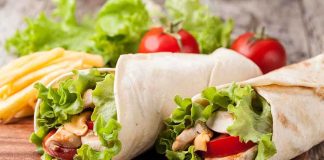 California Dictates Tortilla Ingredients Two chicken wraps filled with lettuce and tomatoes on a wooden plate with fries