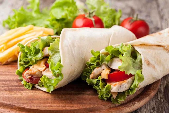 Two chicken wraps filled with lettuce and tomatoes on a wooden plate with fries
