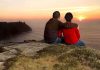 A couple sitting on a cliff watching the sunset over the ocean
