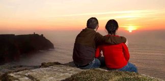 A couple sitting on a cliff watching the sunset over the ocean
