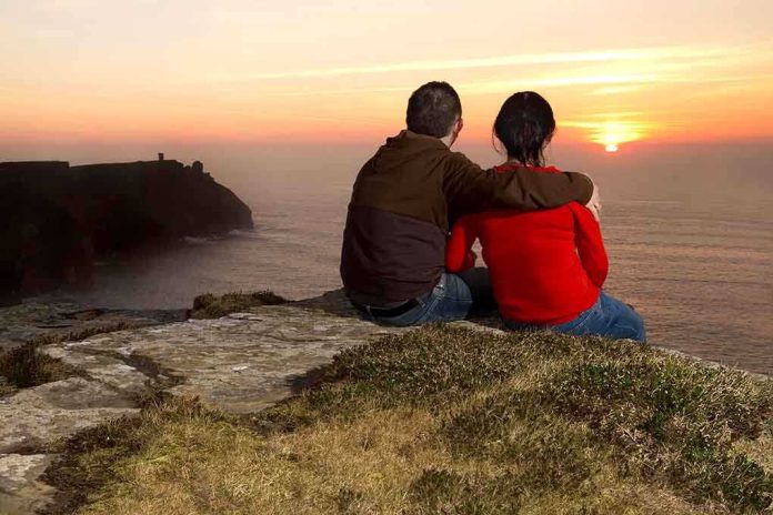shutterstock_72785245.jpg A couple sitting on a cliff watching the sunset over the ocean