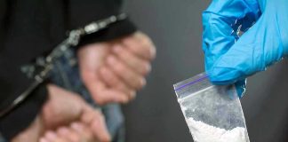 Person handcuffed, police holding bag of white substance.