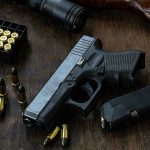 Dad SHOOTS Predator—Arrested Anyway Handgun with ammunition, magazine, and rifle on wooden table.