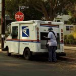 USPS HALTS Pension Payments — Mail Delivery Threatened USPS mail carrier at truck near stop sign.