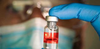 Gloved hand holding vial with red liquid and flag.